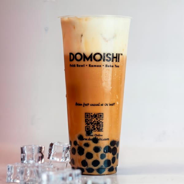 DOMOISHI boba tea with a creamy top layer, dark boba pearls, and ice cubes scattered around.