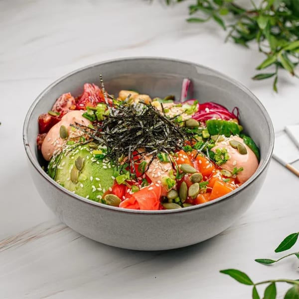 Colorful poke bowl with salmon, avocado, seaweed, and various toppings in a grey bowl.