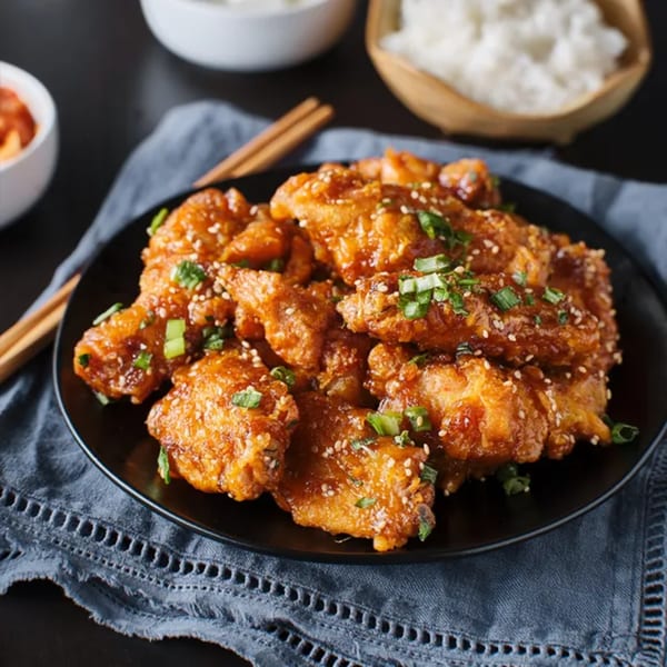 DOMOISHI's crispy orange chicken, garnished with sesame seeds and green onions, served with rice and kimchi.