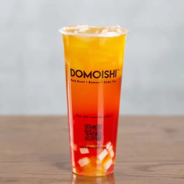 A vibrant, layered DOMOISHI boba tea with yellow and red liquid, topped with fruit pieces.
