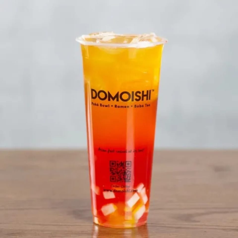 A vibrant, layered DOMOISHI boba tea with yellow and red liquid, topped with fruit pieces.